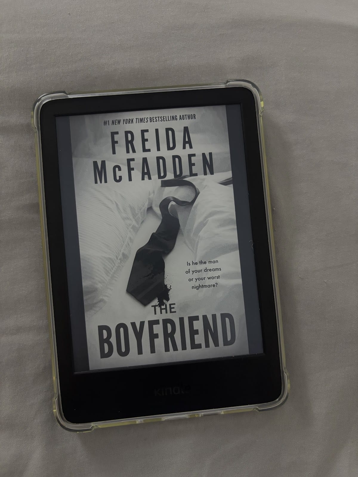 Kindle e-luger, millel on Freida McFaddeni raamatu "The Boyfriend" kaanepilt. Kaanel on must kaelakee valgel voodiplaadil ja tekst, mis kõlab järgmiselt: "Kas ta on sinu unistuste mees või su halvim õudusunenägu?