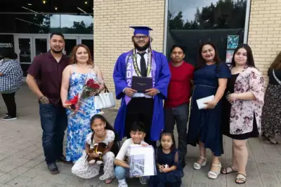 Sinise mütsi ja kleidiga lõpetaja hoiab diplomit, teda ümbritsevad seitse naeratavat pereliiget. Mõned hoiavad lilli ja kaisukaru käes, tähistades õues.